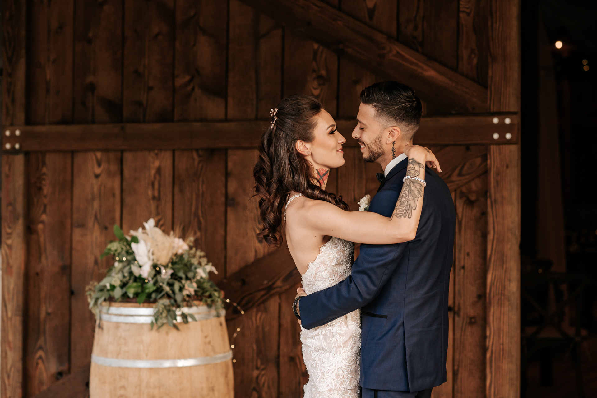 Bride and Groom looking into each others eyes with a boho floral arrangement with pompous grass on a wine barrel in the background