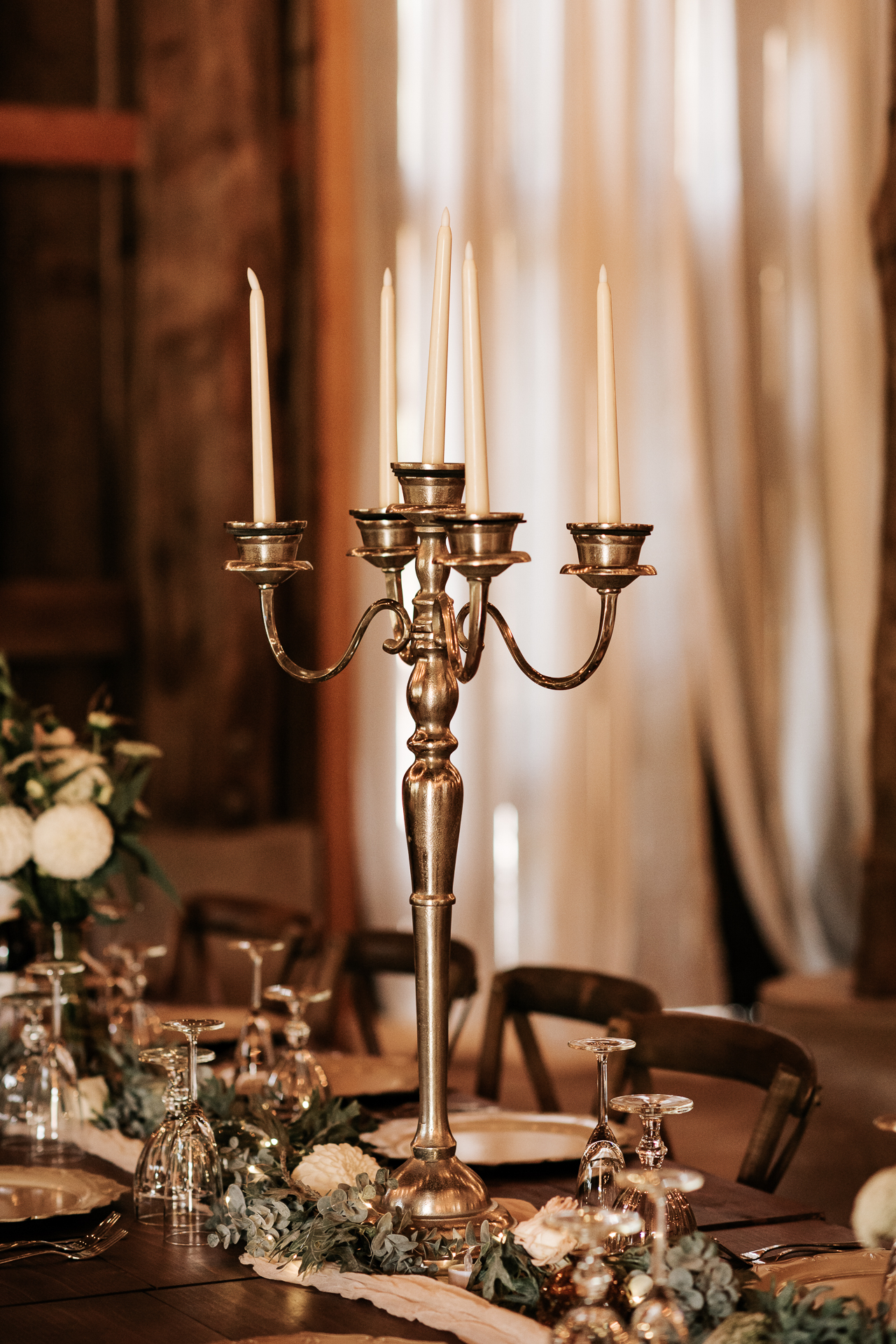 Candle centerpiece on a farm house table at an elegant boho themed barn wedding with glass dinnerware 