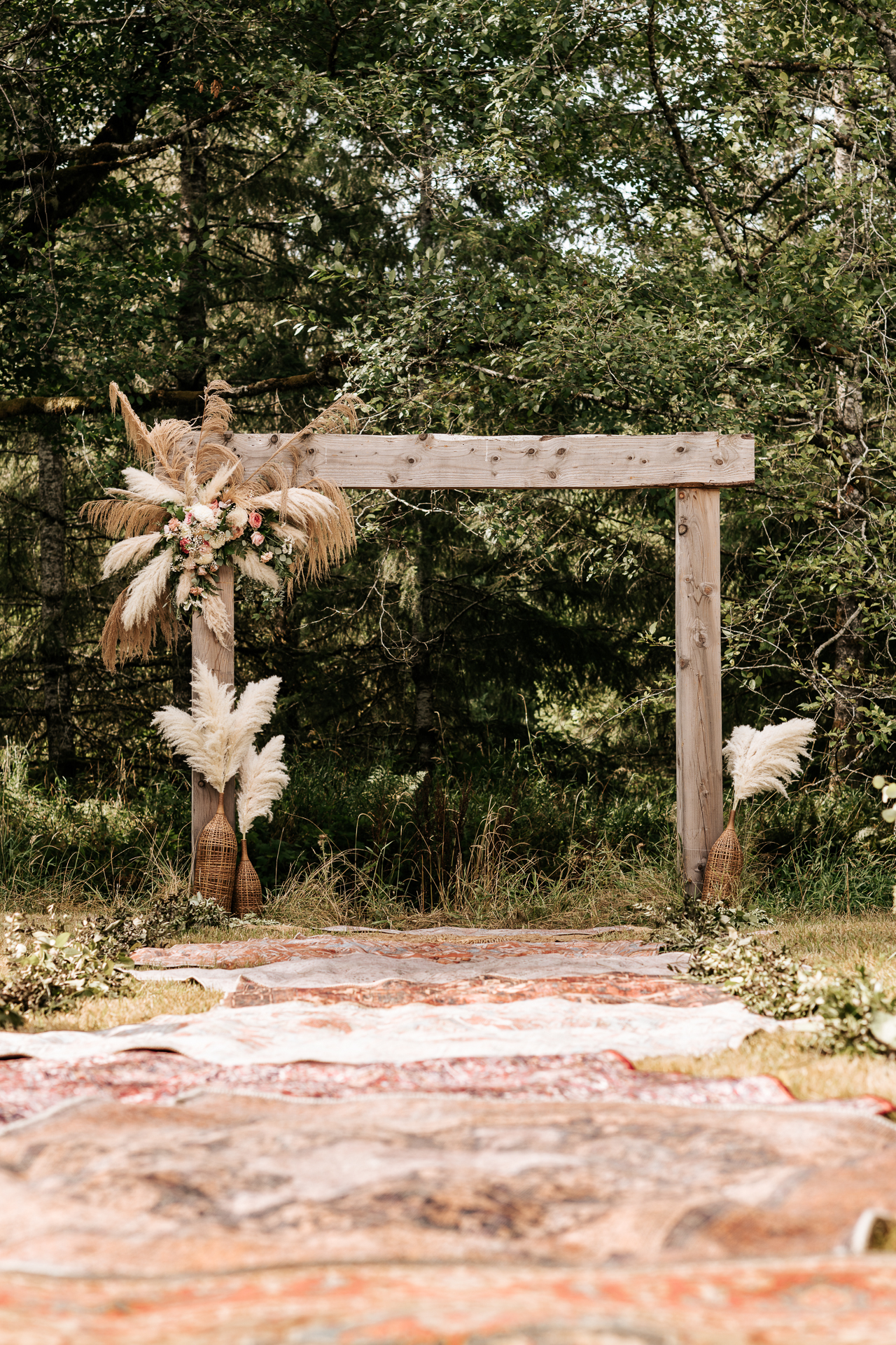 Boho rugs line a wedding ceremony aisle with pompous grass arbor arrangement
