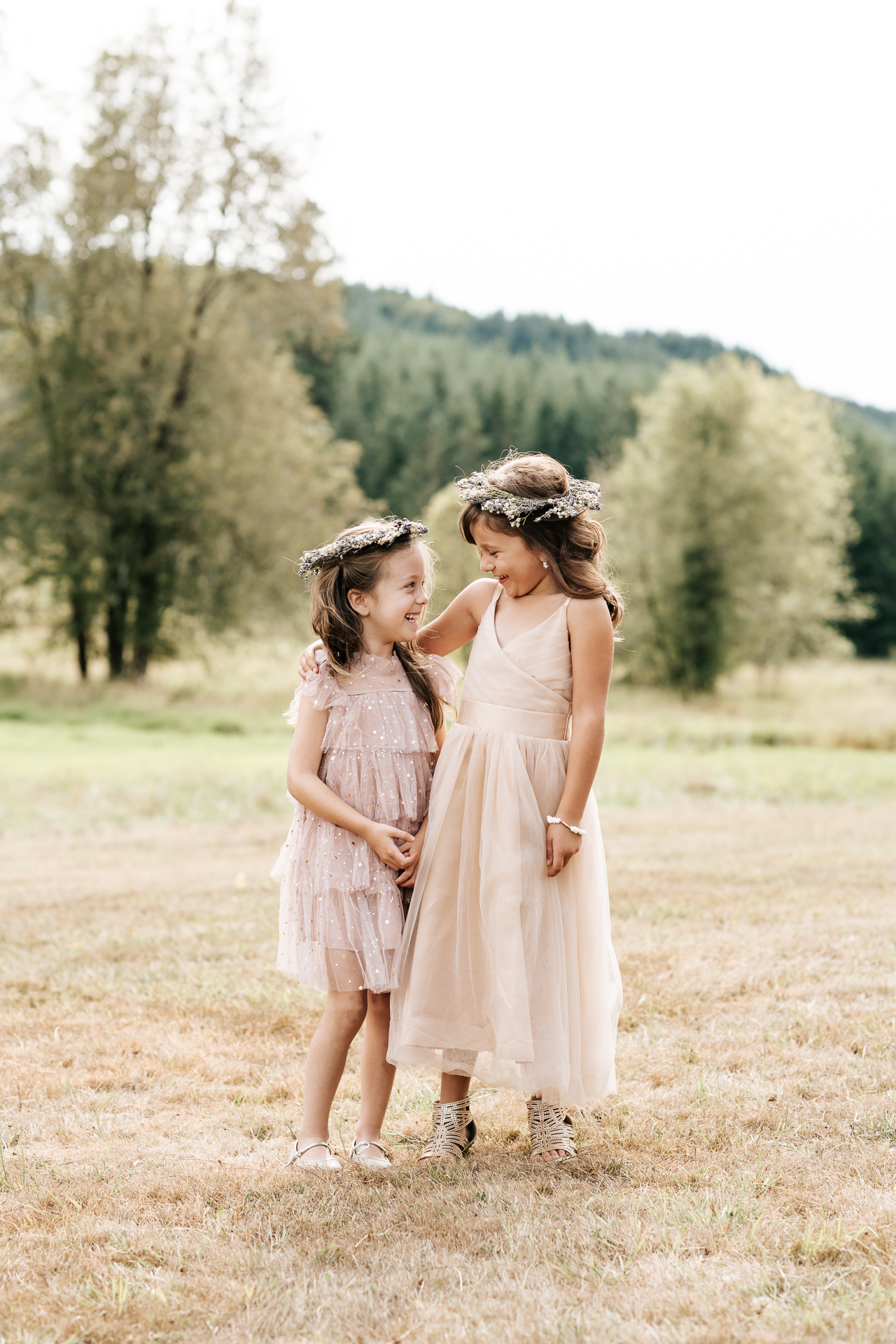 Flower girls giggling to each other wearing dresses and lavender flower crowns
