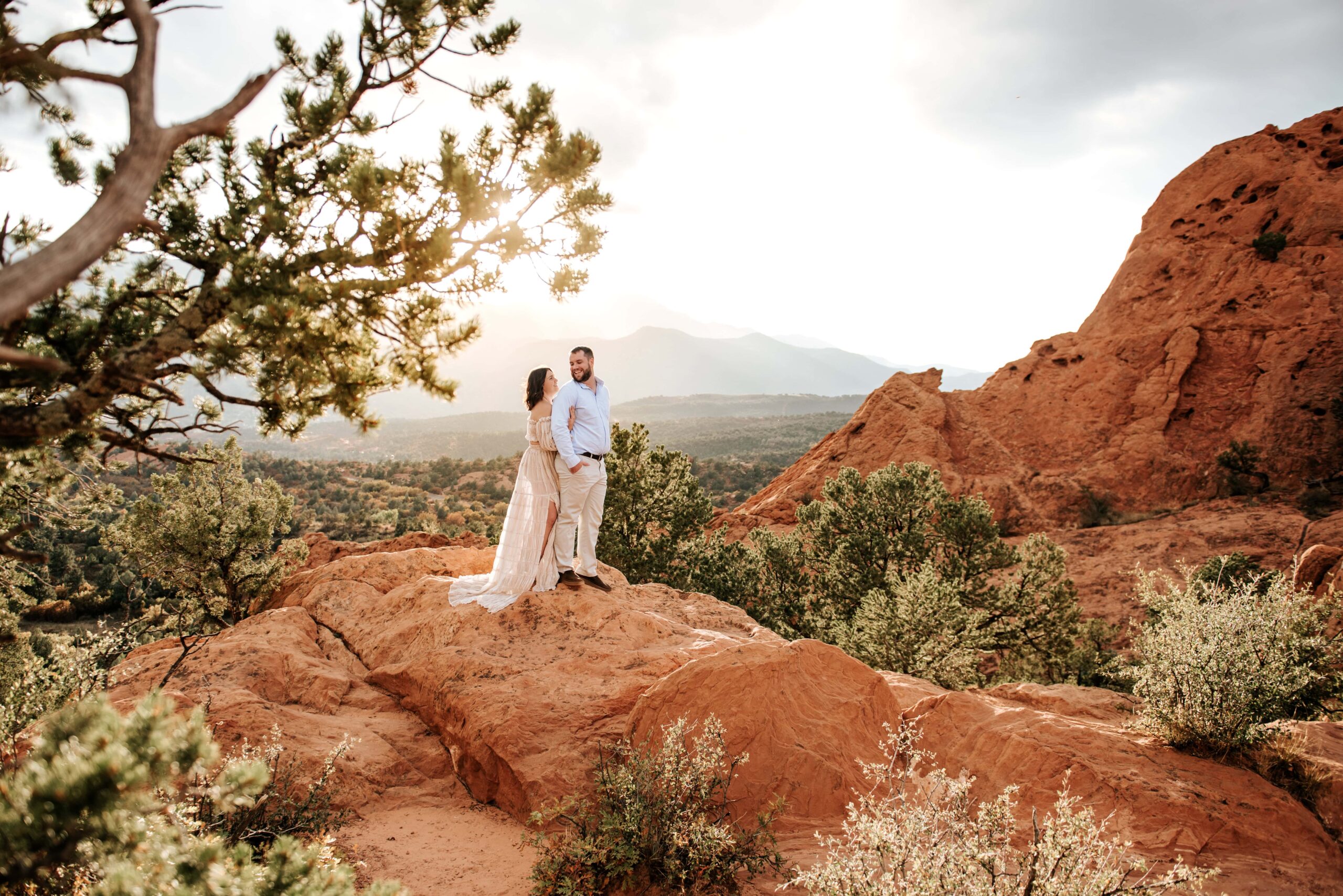 Couple standing on rock formations at Garden of the Gods at sunset with Pikes Peak in the background