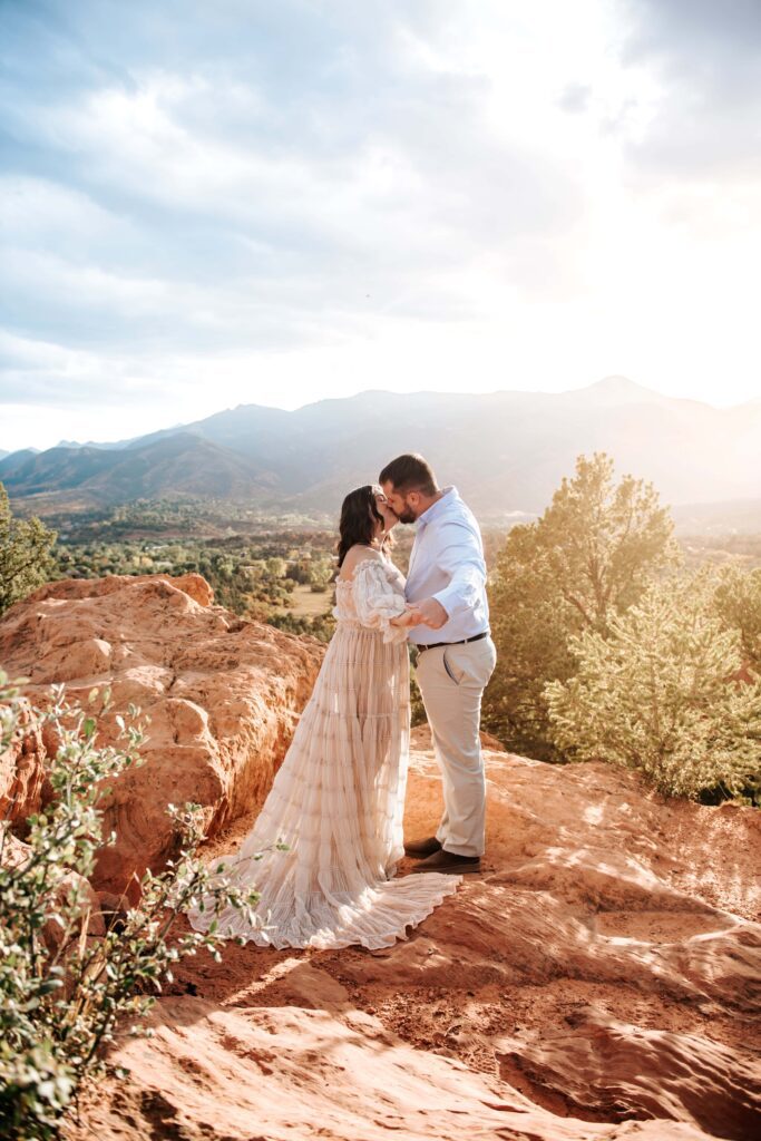 Couple kissing at their engagement session standing on red rock formations at Garden of the Gods
